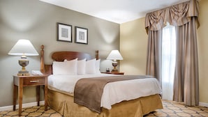 A hotel room with a large bed, two bedside tables with lamps, a wooden headboard, a brown throw blanket, and a patterned carpet. - Club Wyndham Patriots Place (Williamsburg)