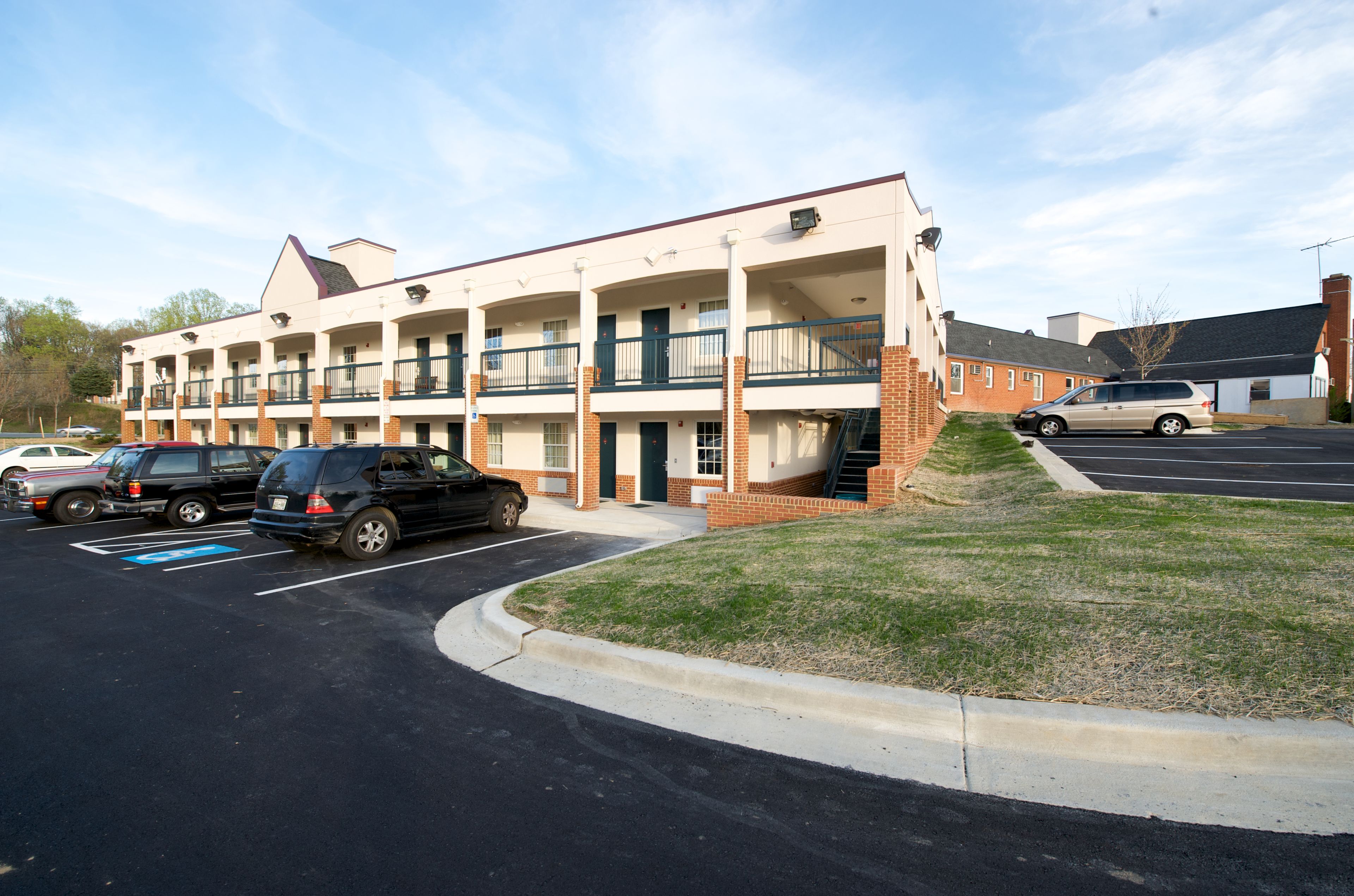 A multi-story motel with a parking lot, a grassy area, and a staircase leading to the upper floors.