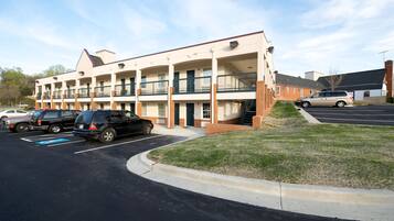 A multi-story motel with a parking lot, a grassy area, and a staircase leading to the upper floors.