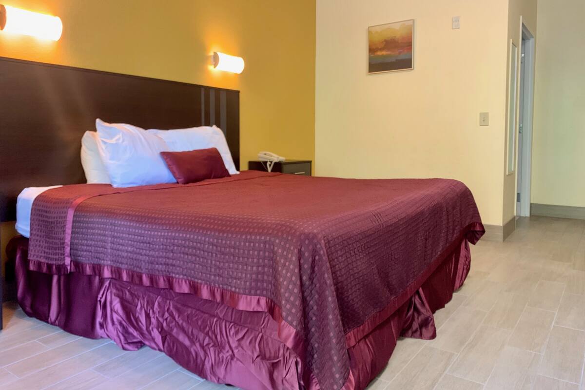 Quarto de hotel com uma cama grande, cabeceira, mesa de cabeceira, telefone e um quadro na parede.