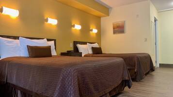 A hotel room with two beds, each with a brown bedspread and white pillows. There are wall-mounted lights on the left side of the room.