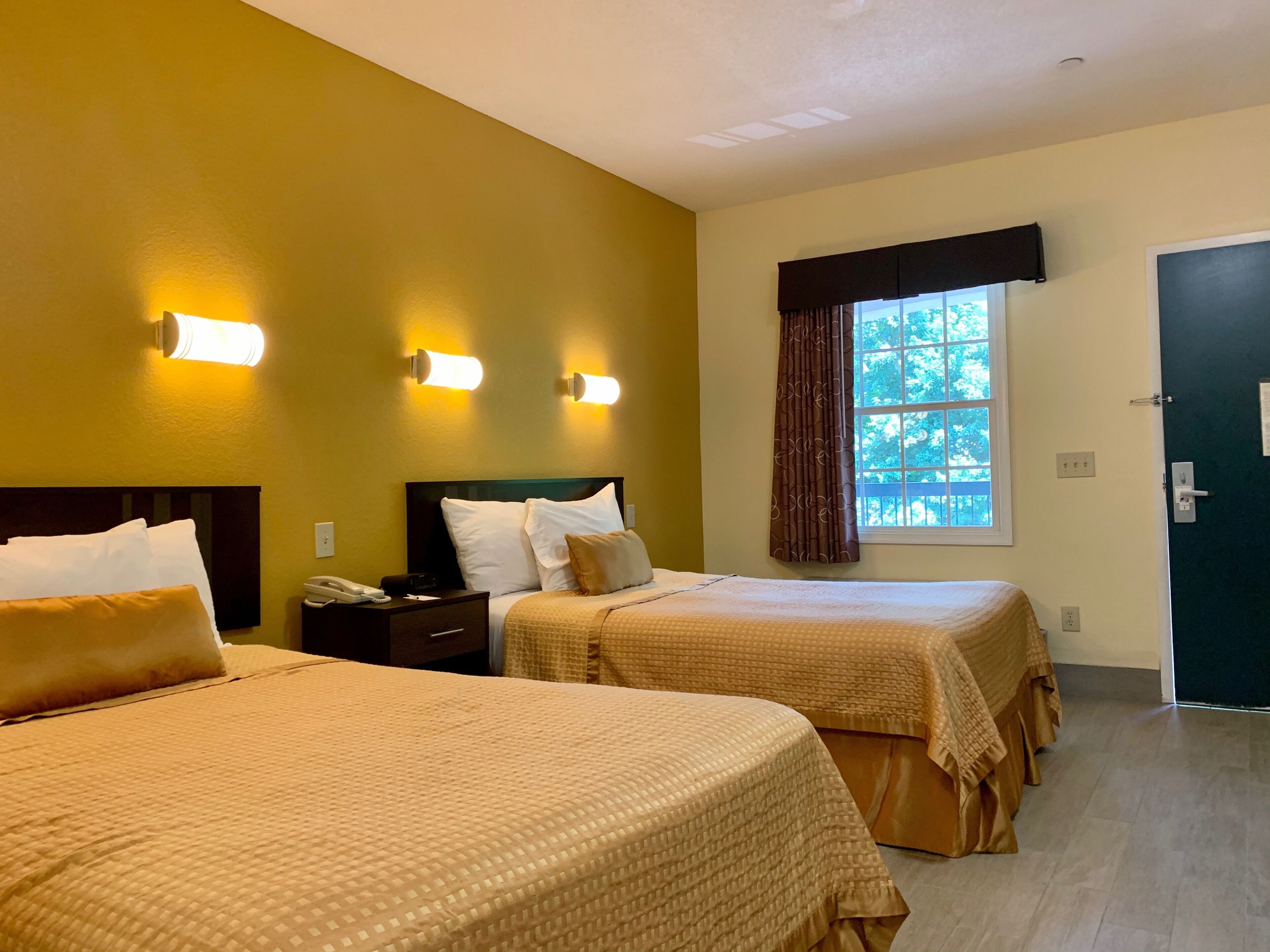 A hotel room with two beds, a nightstand, a telephone, and a window with curtains.