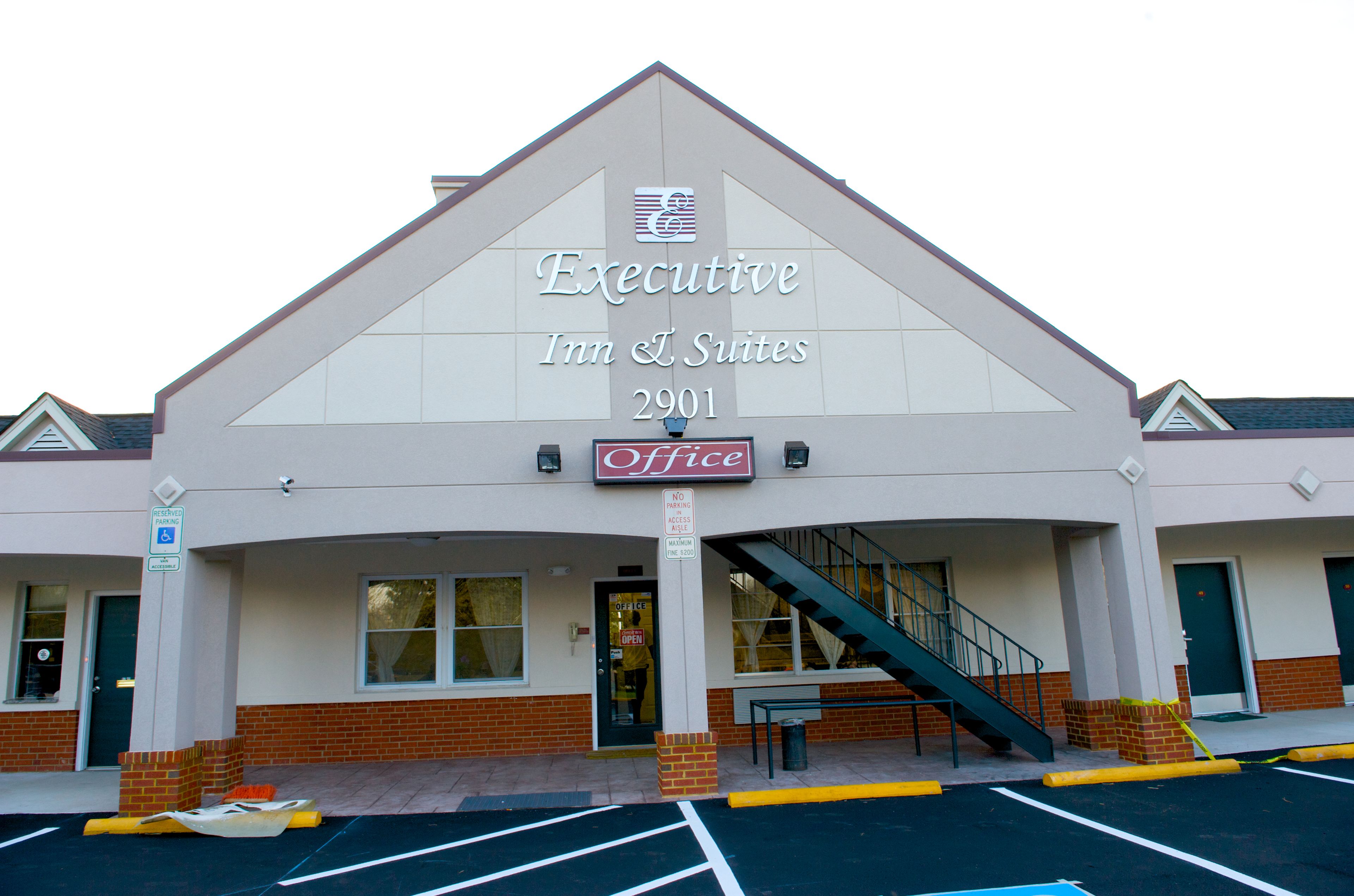 Esterno dell'Executive Inn & Suites 2901, con un ingresso ben visibile, una rampa di scale e un'insegna che indica una reception, oltre a un segnale che indica parcheggio per disabili.