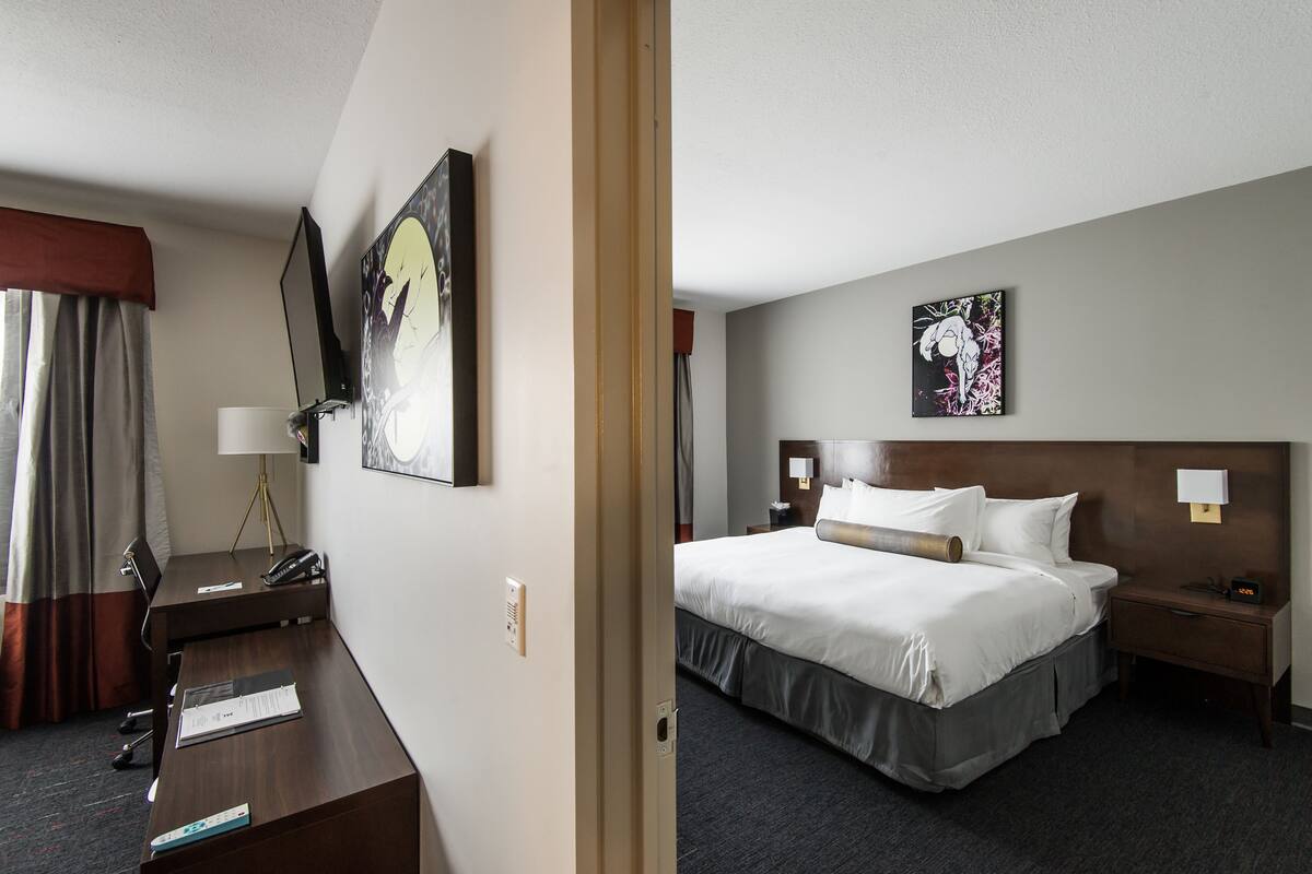 A hotel room with a bed, bedside table, lamp, and a desk with a chair.