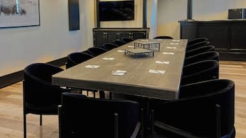 A conference room with a long table, black chairs, a projector screen, and a mounted TV.