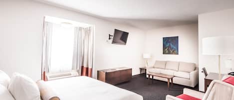 Quarto de hotel com cama, sofá, mesa de centro, televisão e um quadro na parede.