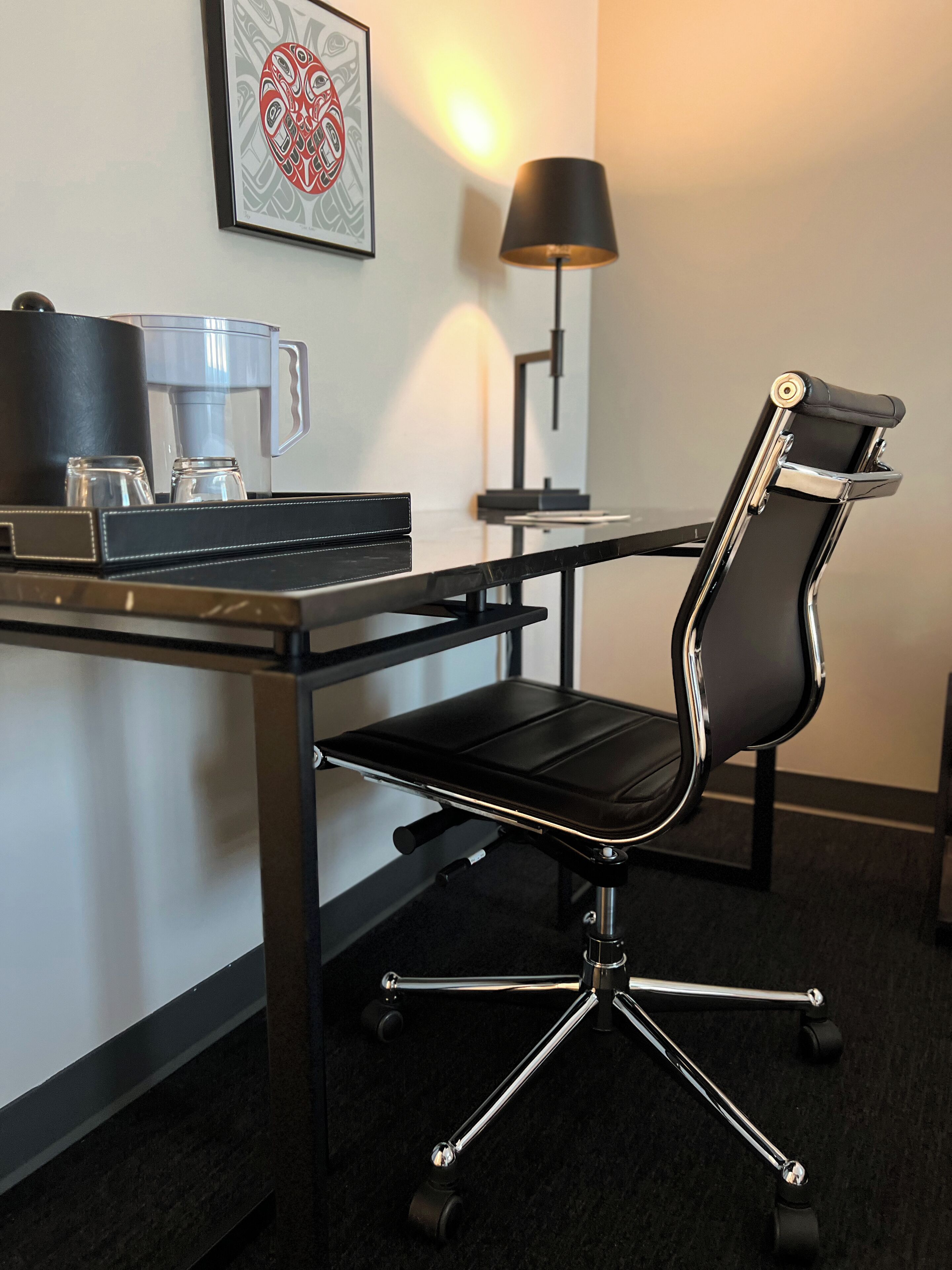 Une chambre d’hôtel moderne, dotée d’un fauteuil en cuir noir, d’une machine à café et d’une œuvre d’art encadrée au mur.