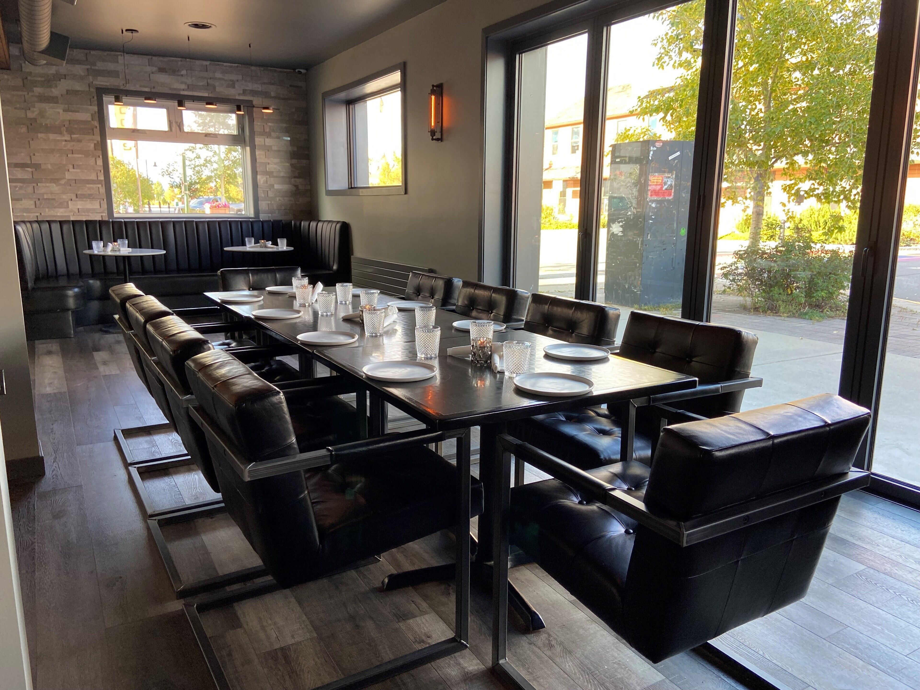 Un restaurant doté d’une longue table conviviale, de banquettes en cuir noir et de grandes fenêtres donnant sur la rue.