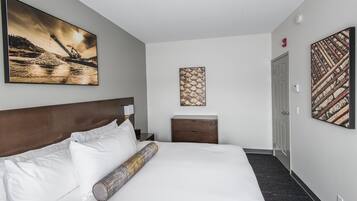 Habitación de hotel con una cama grande, cabecero, mesita de noche, lámpara, mesita auxiliar de madera y dos obras de arte en las paredes.