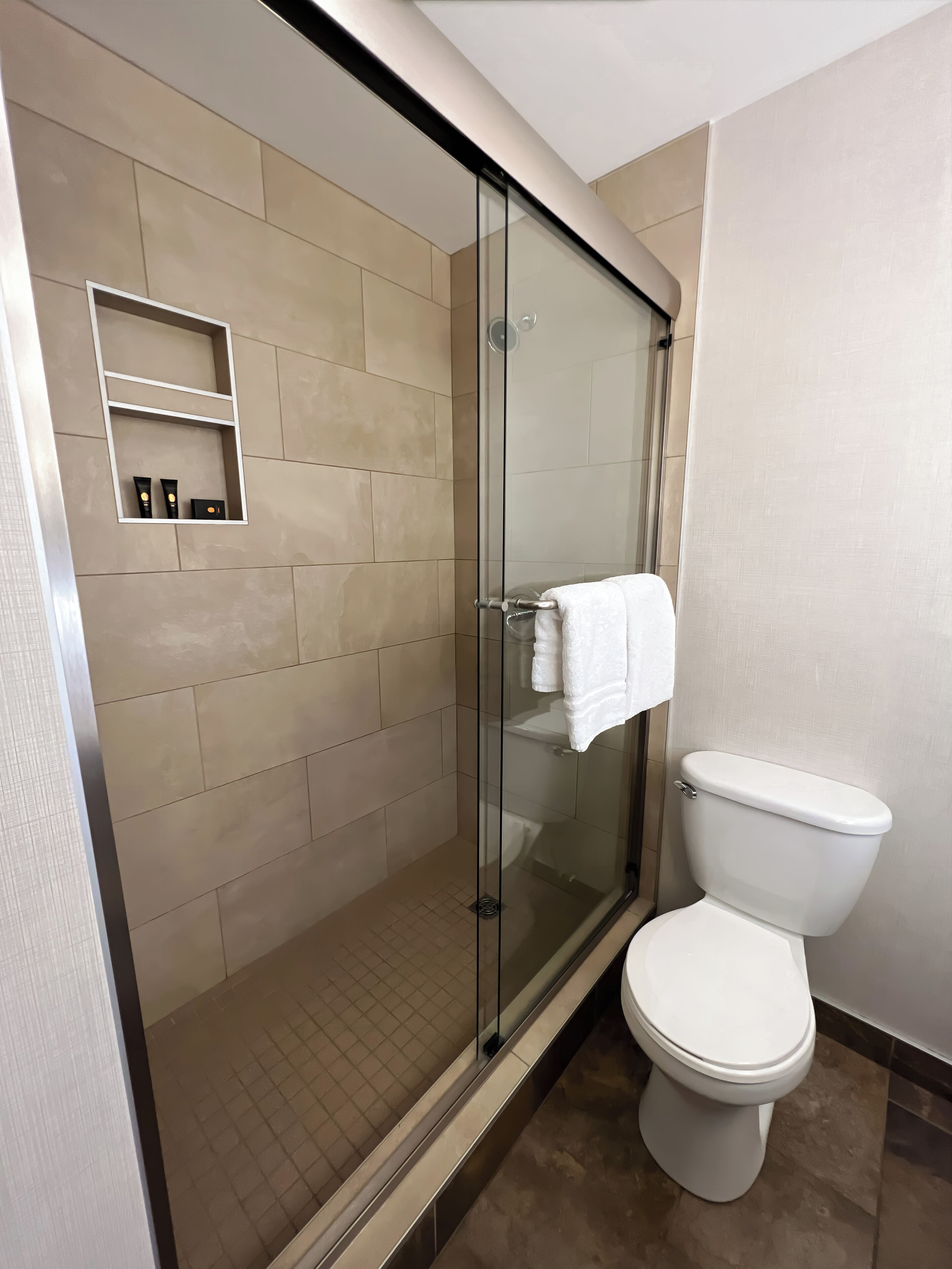 A modern bathroom with a glass-enclosed shower, a white toilet, and beige tiled walls.