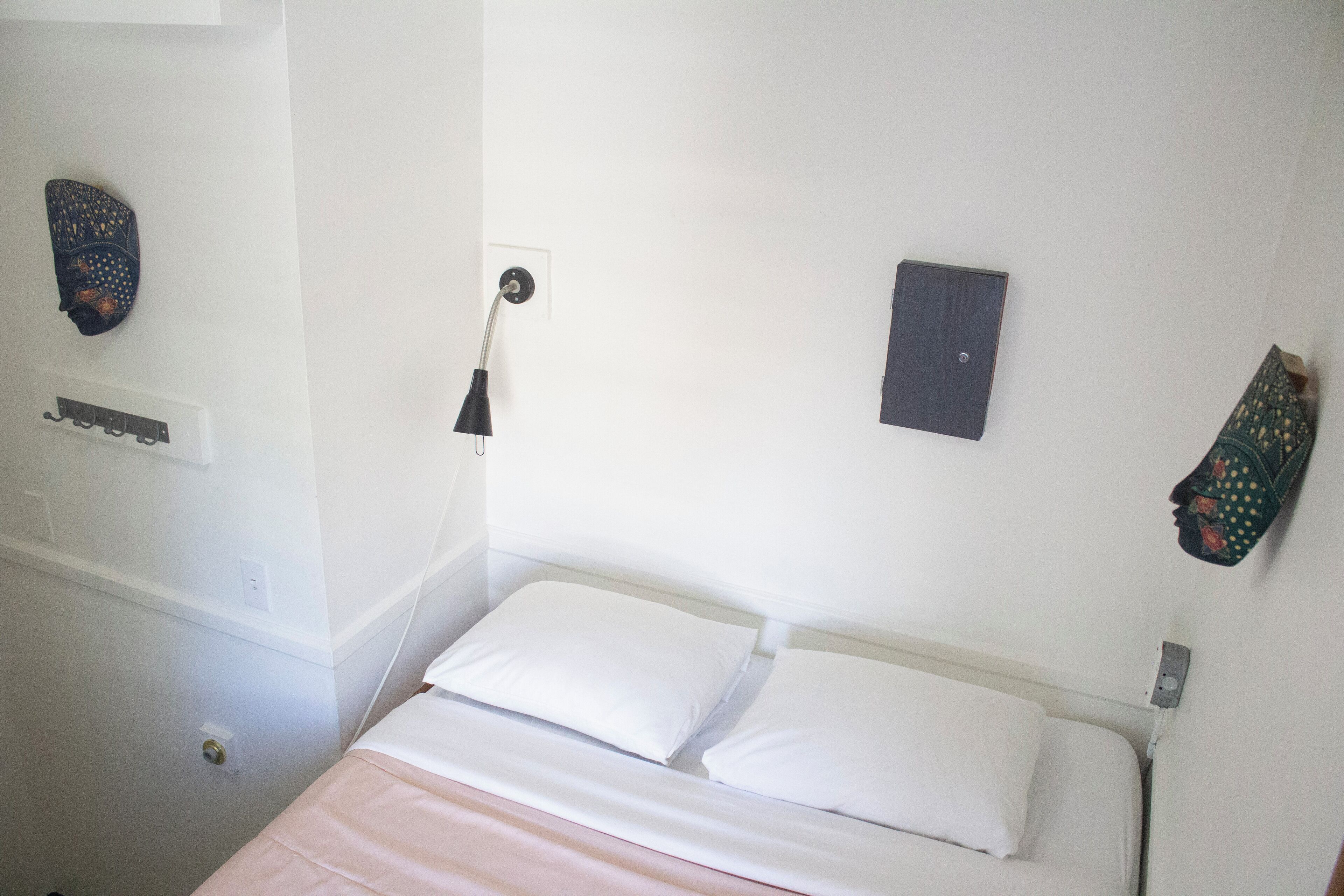 A bedroom with a bed, two pillows, a bedside lamp, and a wall-mounted shelf.