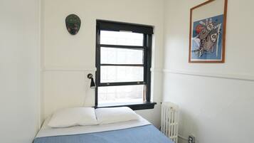 A bedroom with a single bed, a window with black frames, a radiator, and a wall-mounted artwork.
