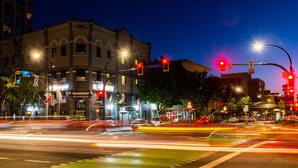A street view at night with traffic lights, street signs, and illuminated buildings.