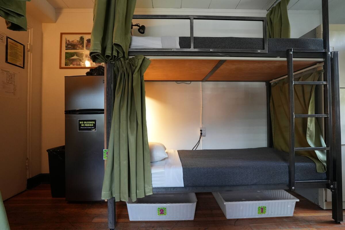 Une chambre avec des lits superposés, un réfrigérateur, une poubelle et un tableau accroché au mur.