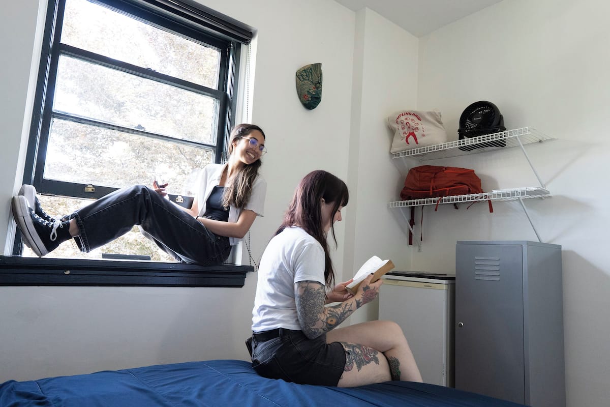 Une chambre de dortoir équipée d’un lit, d’une fenêtre, d’un radiateur et d’un casier en métal.