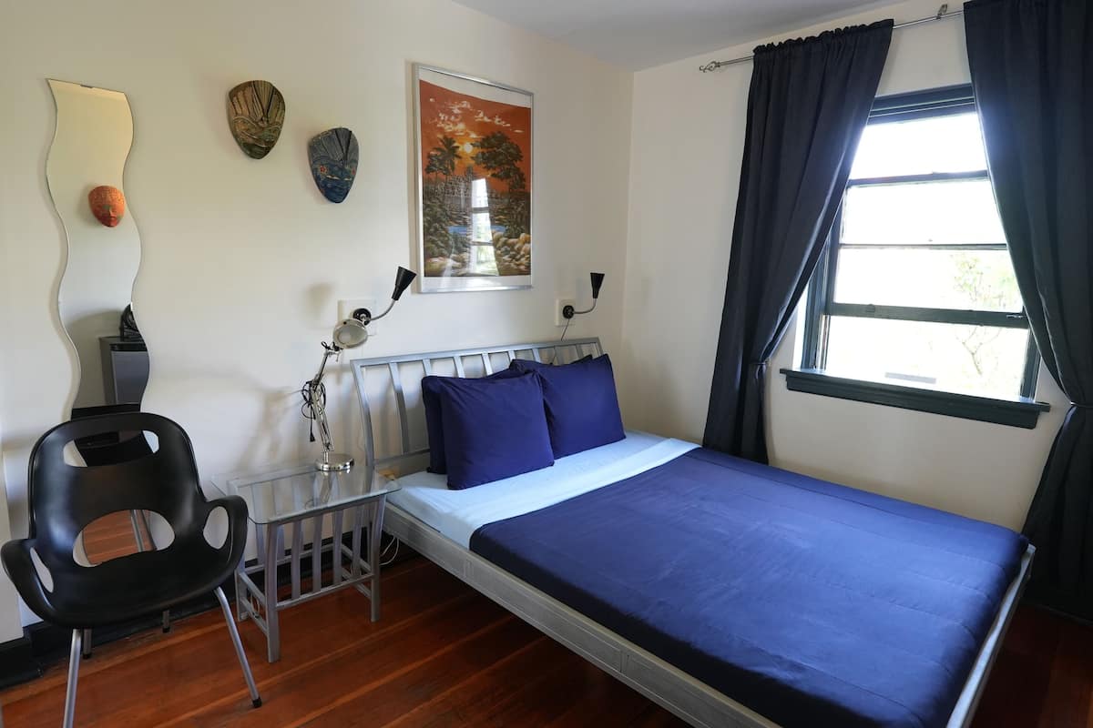 Une chambre à coucher comprenant un lit, une chaise, une petite table, une lampe et des œuvres d’art murales.