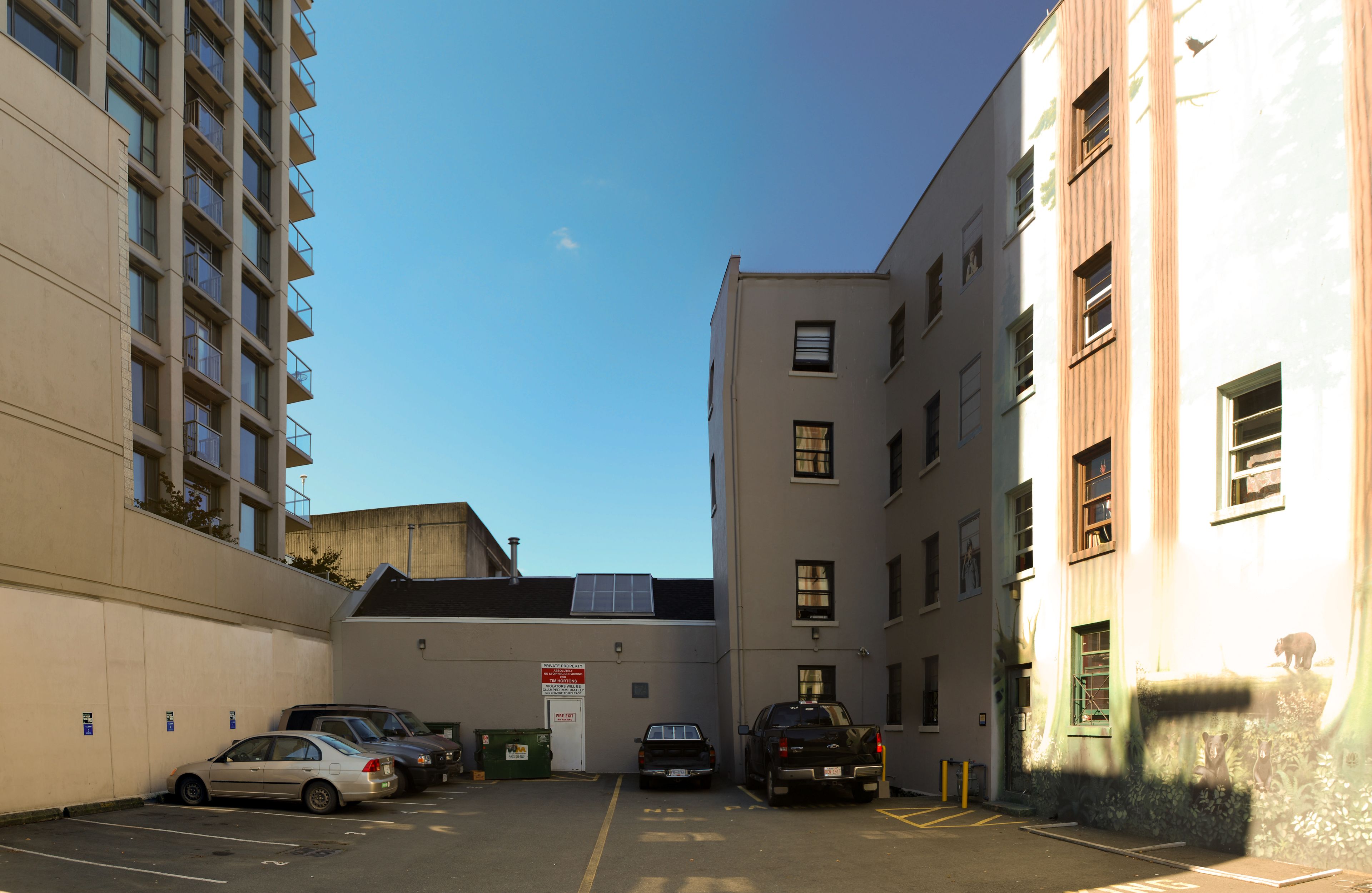A parking lot with several cars and a truck, adjacent to a building with multiple windows and balconies.