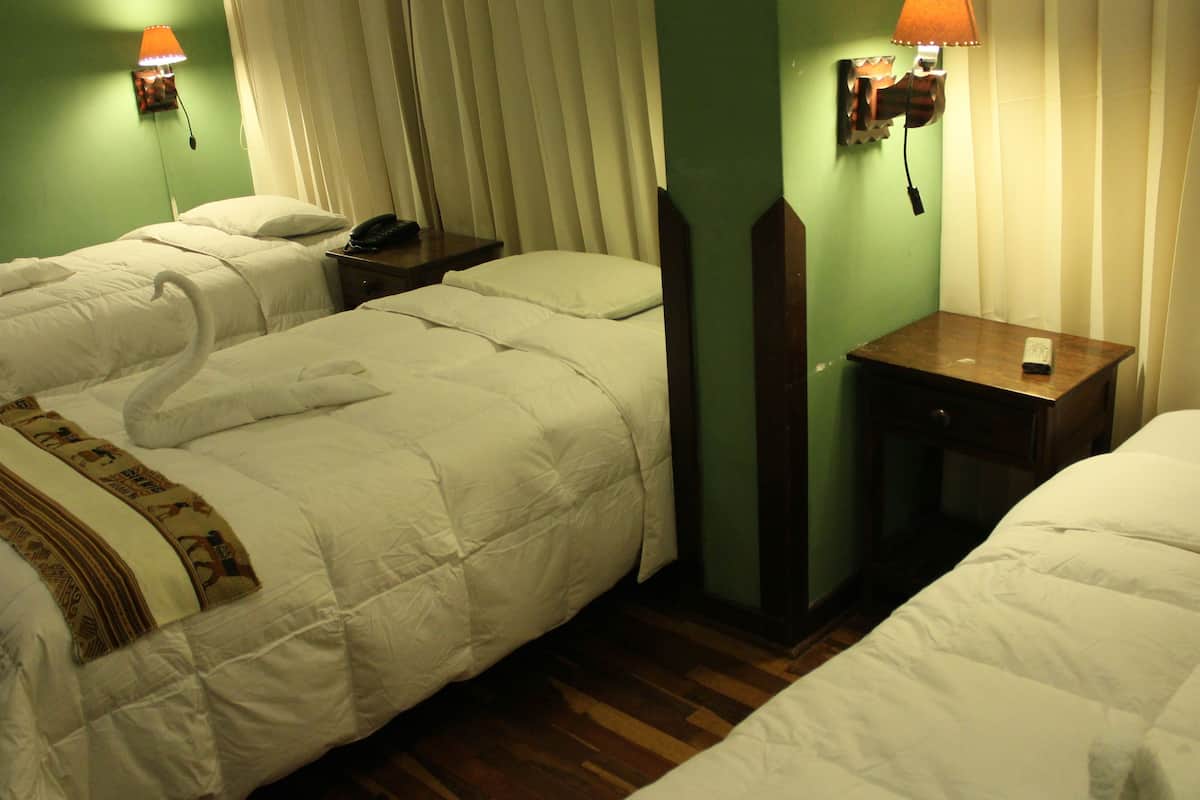Une chambre d’hôtel avec deux lits, chacun agrémenté d’un oreiller en forme de cygne, une table de chevet avec une lampe et une petite table de nuit avec un téléphone.