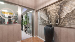 A reception area with a large elephant sculpture, a reception desk, and a glass door leading to the interior. - Hotel Romerito (Málaga)