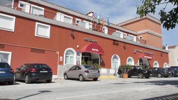 Un hotel con fachada roja, varias banderas y un cartel que indica un restaurante. Hay varios coches estacionados al frente.