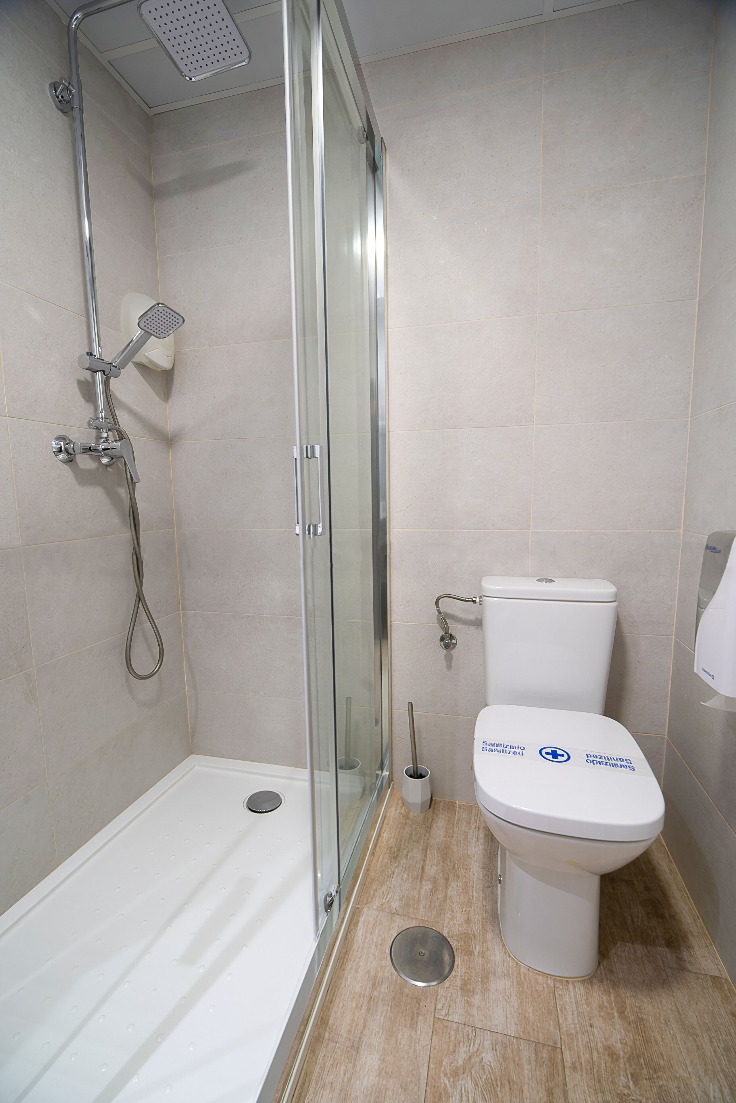 A bathroom with a glass-enclosed shower, a white toilet, and a hand dryer.
