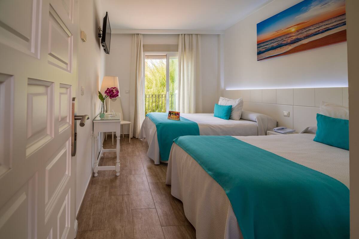 Habitación de hotel con dos camas, una mesita de noche, una lámpara y un cuadro en la pared.