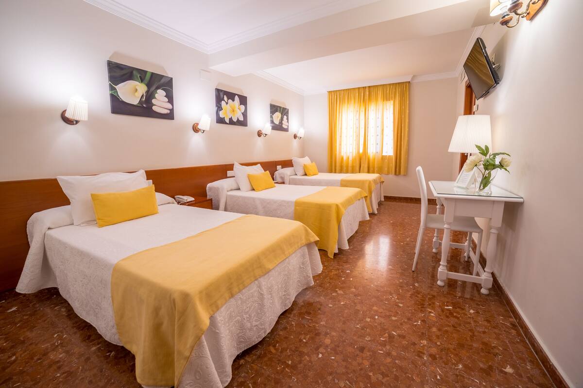 Habitación de hotel con tres camas, un escritorio y una silla.