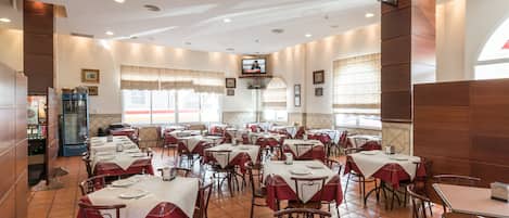 A restaurant with multiple tables and chairs, a television mounted on the wall, and a tiled floor.