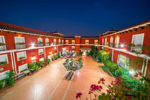 A courtyard with red buildings, potted plants, and a central fountain.