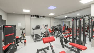 Een sportschool met diverse fitnessapparaten, waaronder loopbanden, krachtapparaten en banken.