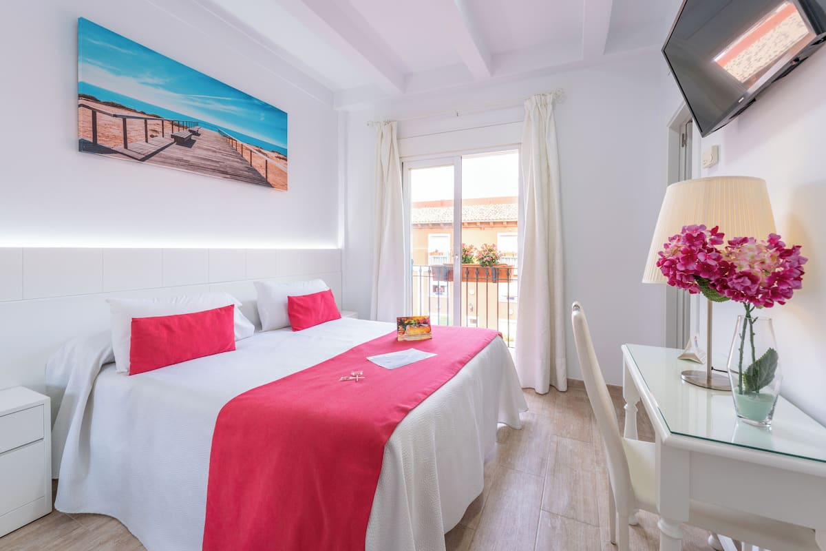 Habitación de hotel con cama, escritorio, televisor y ventana con cortinas.