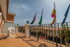 A balcony with a tiled floor, white plastic chairs, and a railing.