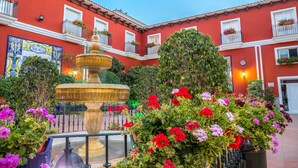 A courtyard with a fountain, potted plants, and a building with balconies. - Hotel Romerito (Málaga)