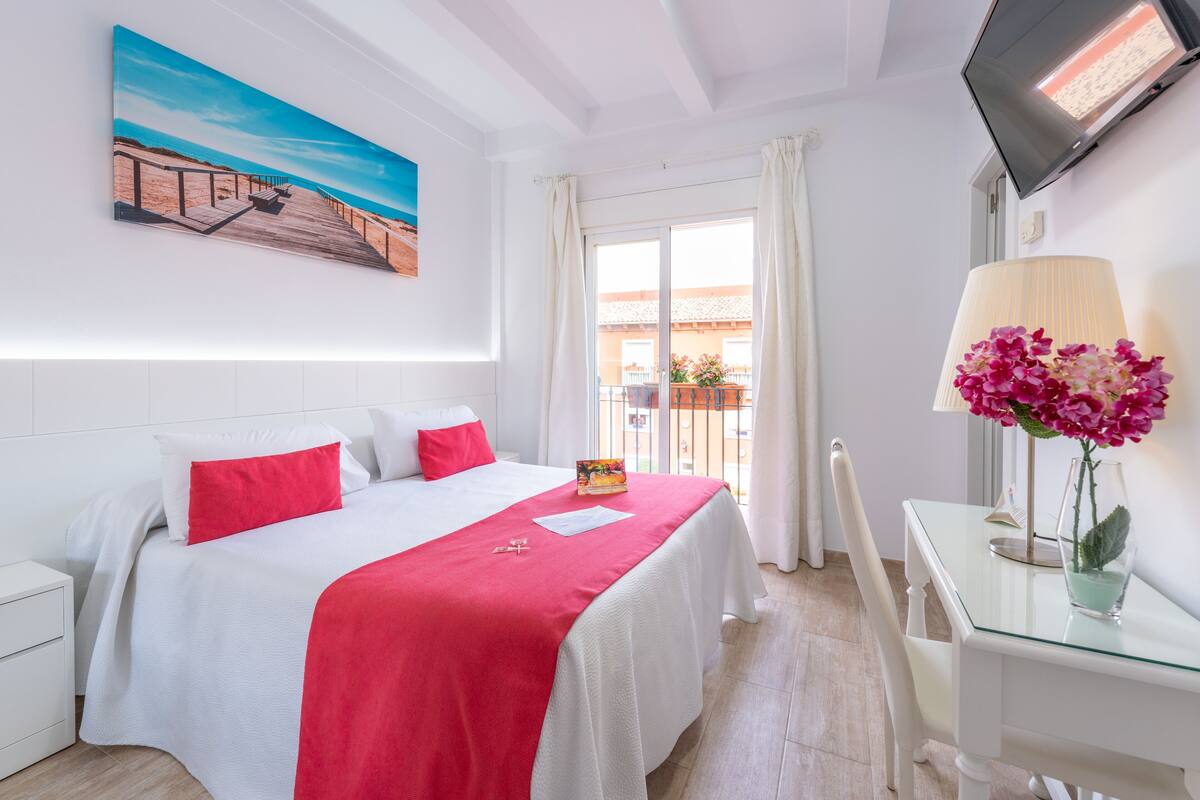 Habitación de hotel con cama, escritorio, televisor y ventana con cortinas.