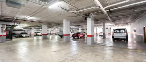 Un estacionamiento con varios niveles, pisos y columnas de concreto, con varios autos estacionados y señalización visible.