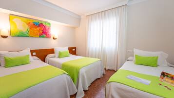 Habitación de hotel con dos camas, cada una con cubrecama verde y almohadas blancas. En la pared, un cuadro abstracto de colores; una ventana con cortinas blancas y una lámpara en la mesita de noche.