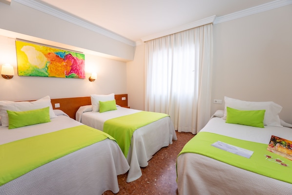 Habitació d'hotel amb dos llits, cadascun amb estovatge verd i almoades blanques. A la paret hi ha un quadre abstracte i colorit, una finestra amb cortines blanques i una làmpada a la tauleta de nit.
