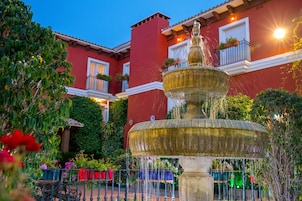 Una fuente de varios niveles en un patio con un edificio rojo al fondo.