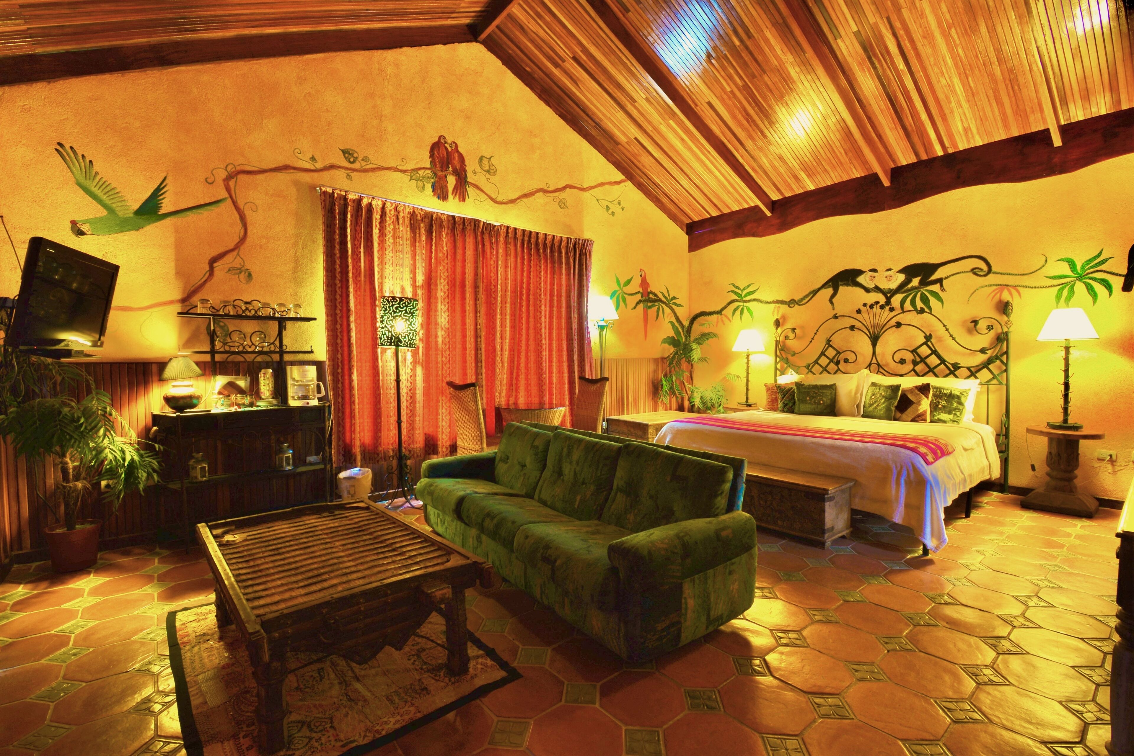 A cozy room with a bed, green sofa, wooden coffee table, and a TV on a shelf.