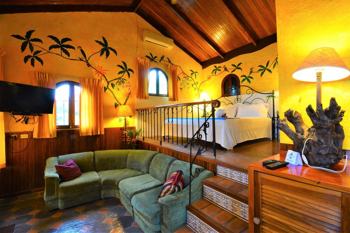 Una habitación acogedora con un sofá verde, una cama, una escalera de madera y un televisor.