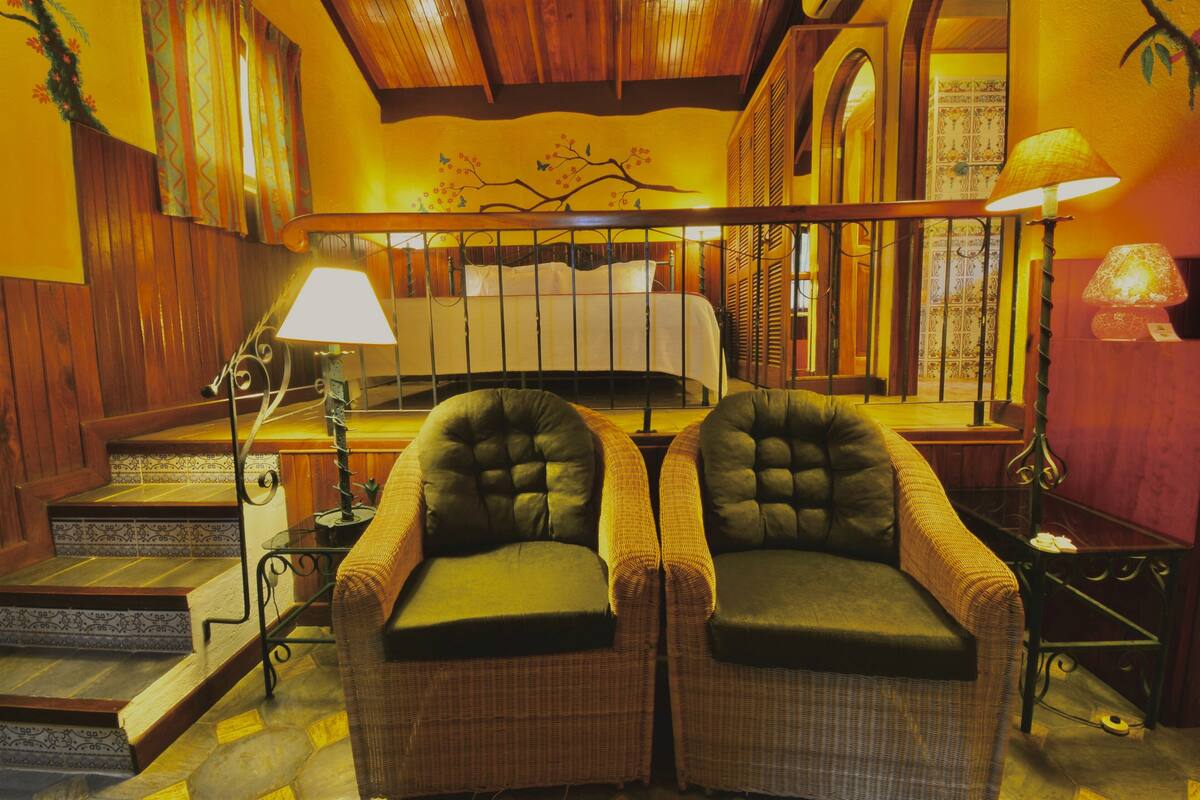 Una habitación acogedora con una cama, dos sillones, una lámpara y una escalera.