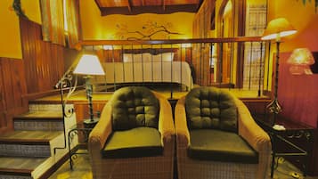 A cozy room with a bed, two armchairs, a lamp, and a staircase.