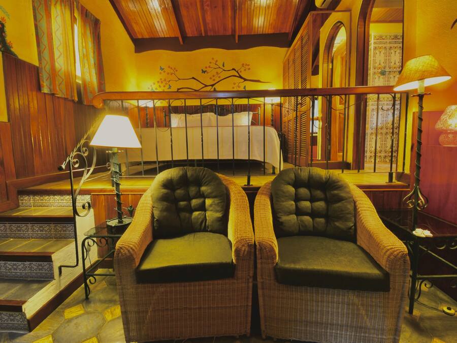 A cozy room with a bed, two armchairs, a lamp, and a staircase.