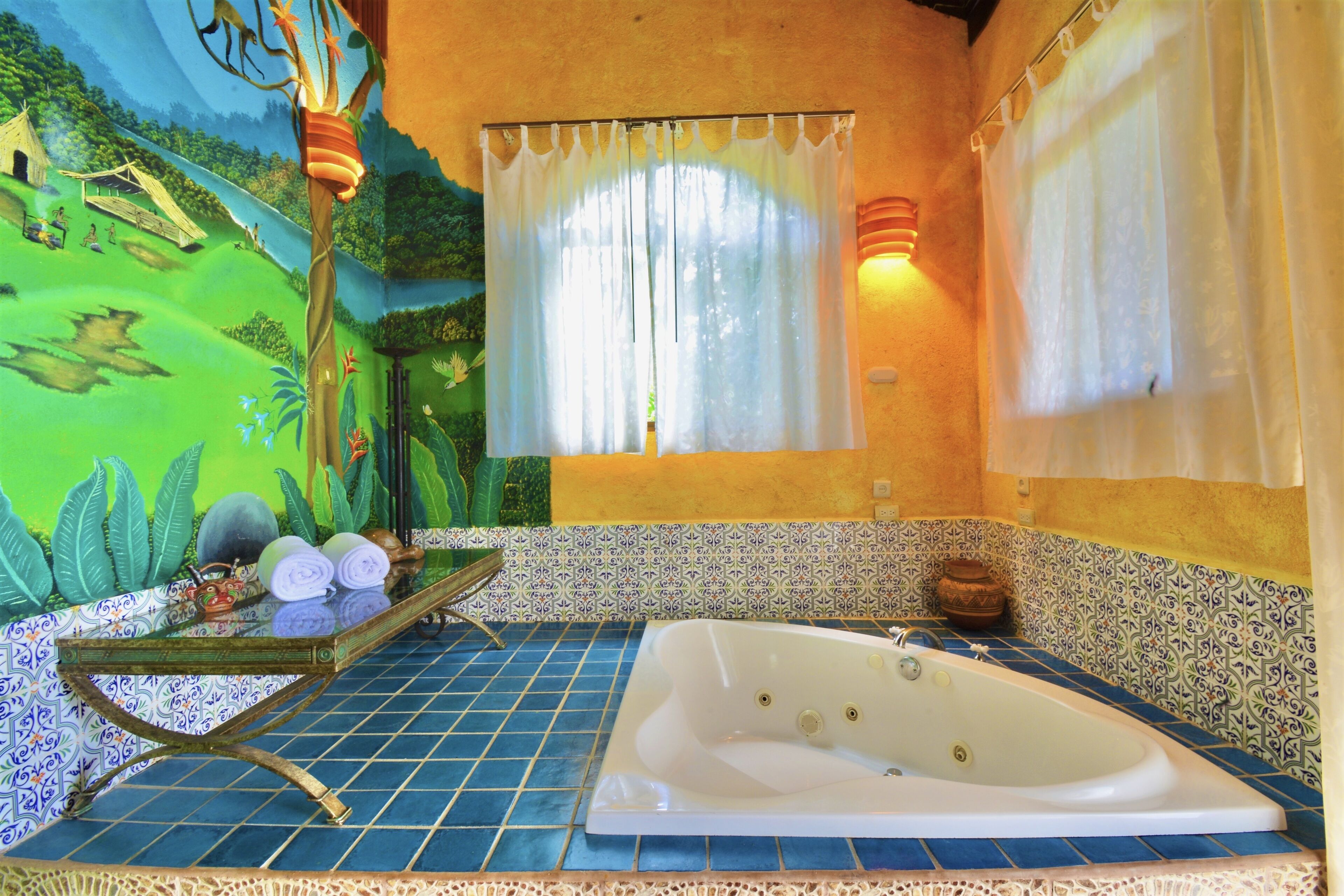 A bathroom with a large bathtub, a mural on the wall, and a window with curtains.