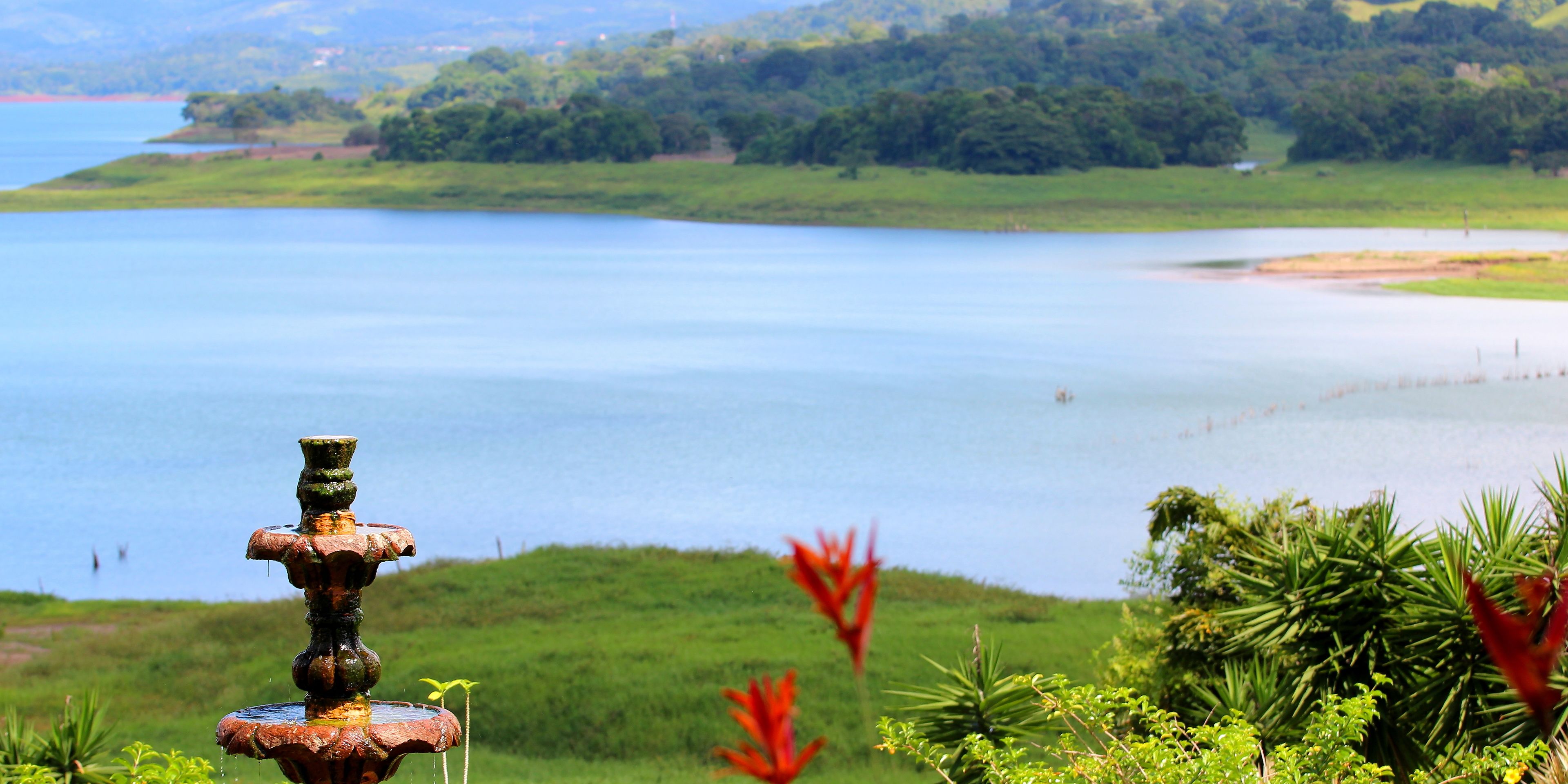A rustic water fountain in a lush landscape with a lake and greenery in the background.