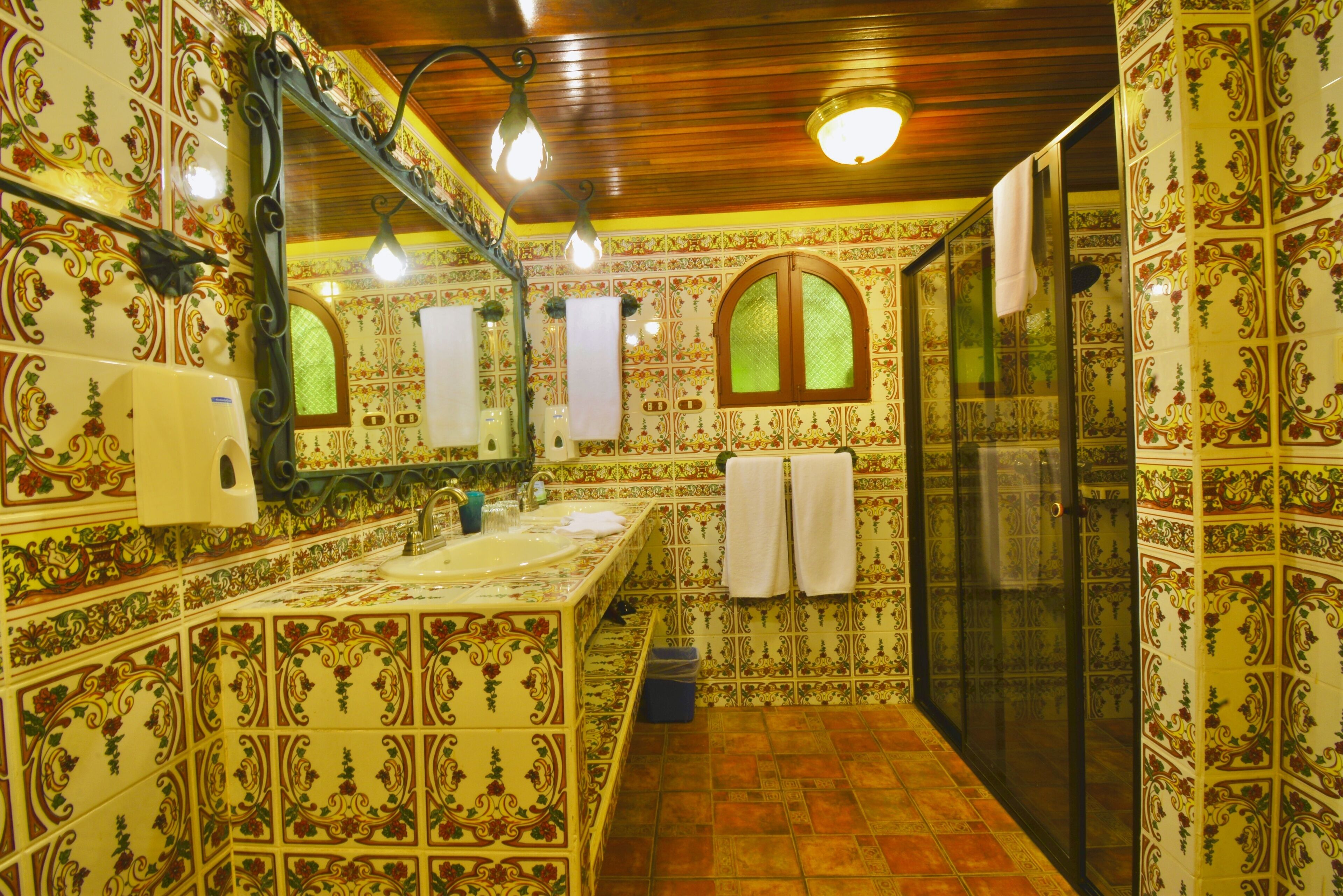 Une salle de bain aux murs recouverts de carreaux décoratifs, avec un lavabo, un miroir et un espace douche.