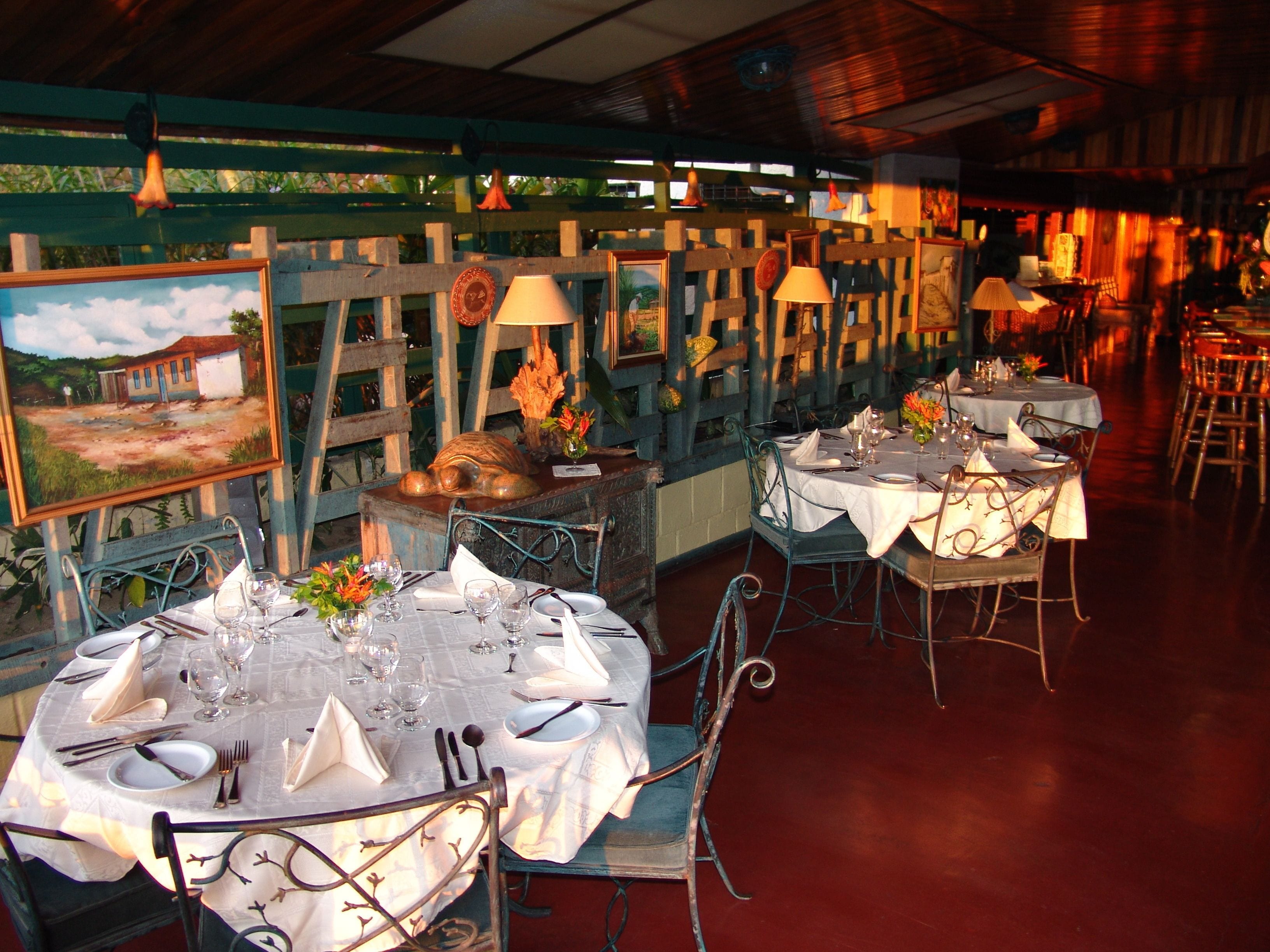A restaurant with round tables set for dining, featuring white tablecloths and metal chairs.