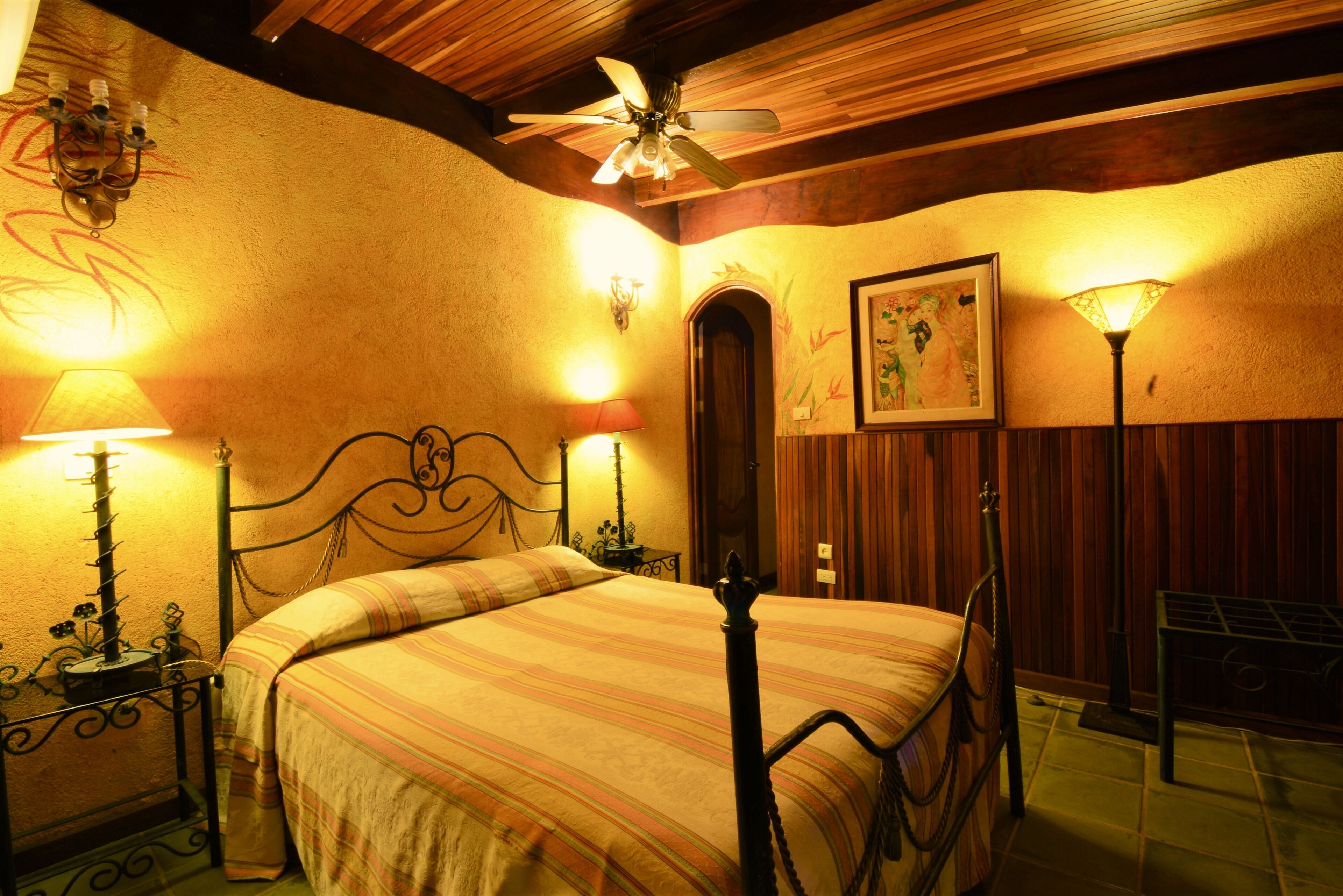 A bedroom with a bed, two bedside lamps, a ceiling fan, and a wall-mounted picture.