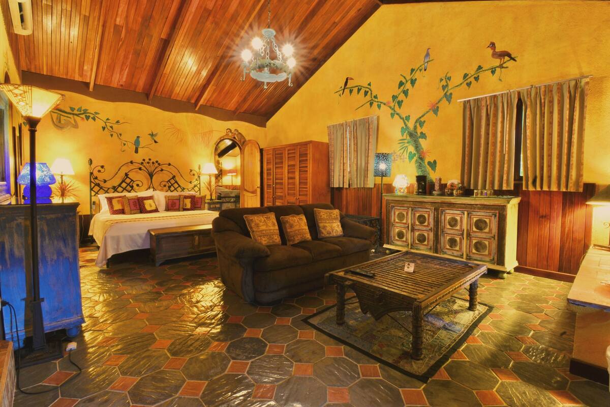 Habitación acogedora con cama, sofá y mesa de centro. El techo es de madera y una pared presenta un mural.