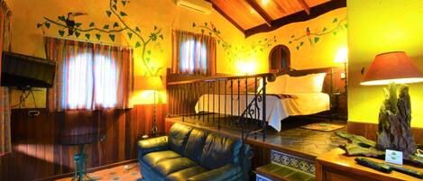 A cozy room with a leather sofa, a bed with a wooden headboard, a staircase with patterned steps, and a wall with a nature-themed mural.